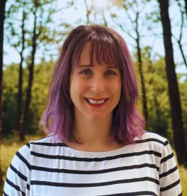 A woman in a black and white striped shirt outside with trees in the background.